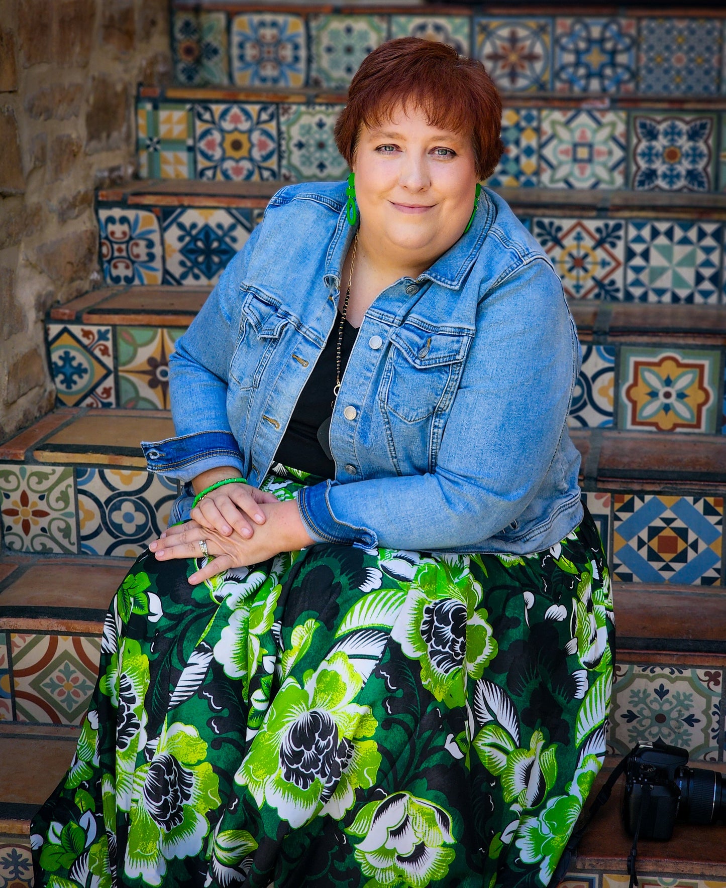 Woman sitting on a decorative staircase with a floral dress and denim jacket.