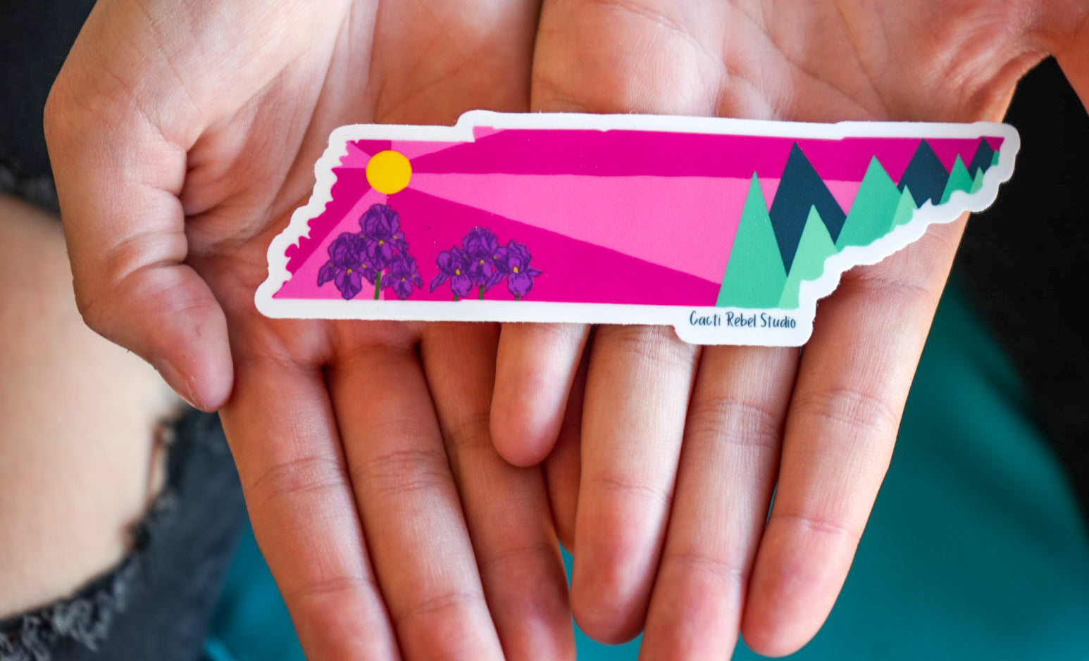 Hand holding a colorful sticker with nature design on a blurred background